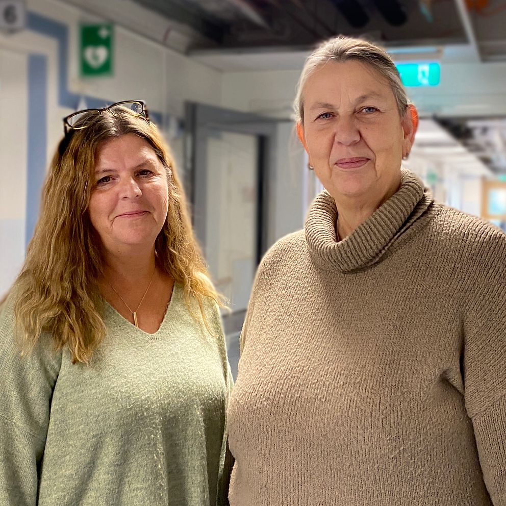 Två personer står i en sjukhuskorridor, klädda i komfortabla tröjor. Korridoren har flera dörrar och släpljus som ger en lugn atmosfär. Bakgrunden är suddig men visar att det är en vårdmiljö.