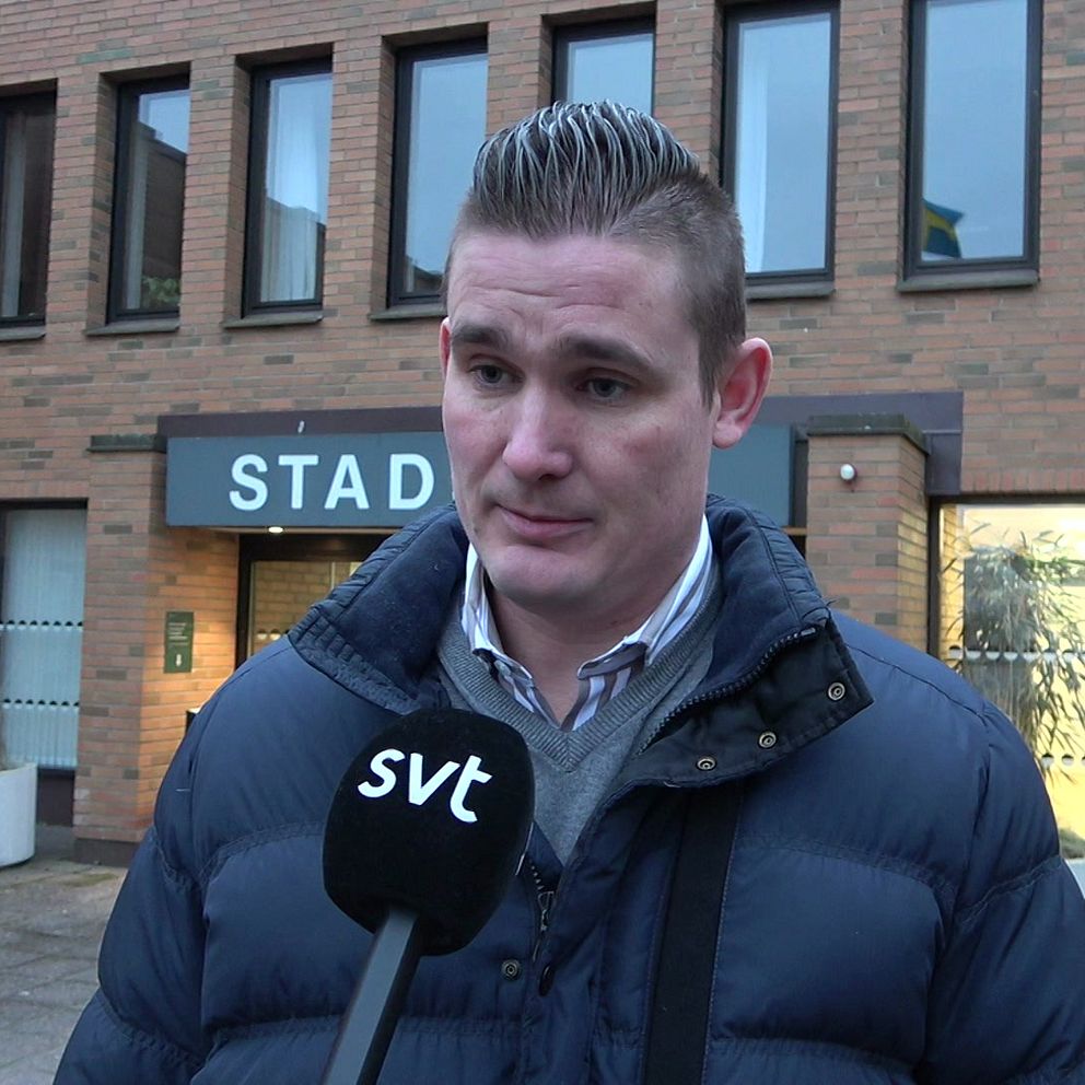 En person står framför en byggnad märkt med ”STAD”, klädd i en mörk dunjacka, och håller en mikrofon från SVT.