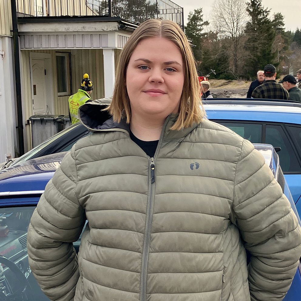 kvinna med grön jacka framför blåa bilar
