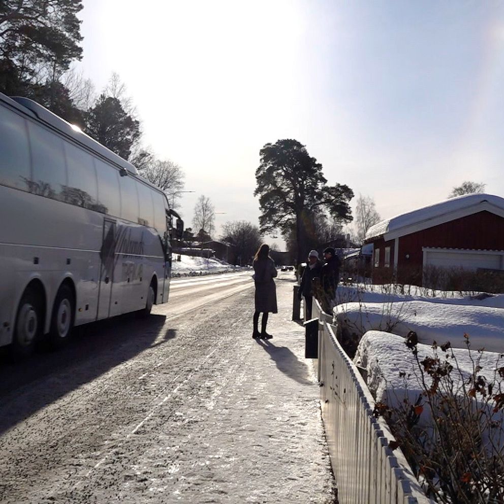 En buss kör förbi nära några som står på en trottoar
