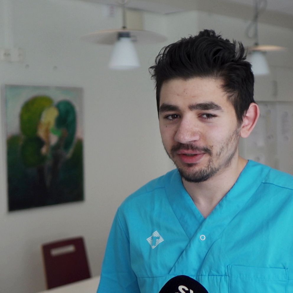 Lokalvårdaren Karam Hatem står med blå kläder i sitt kontor och ler