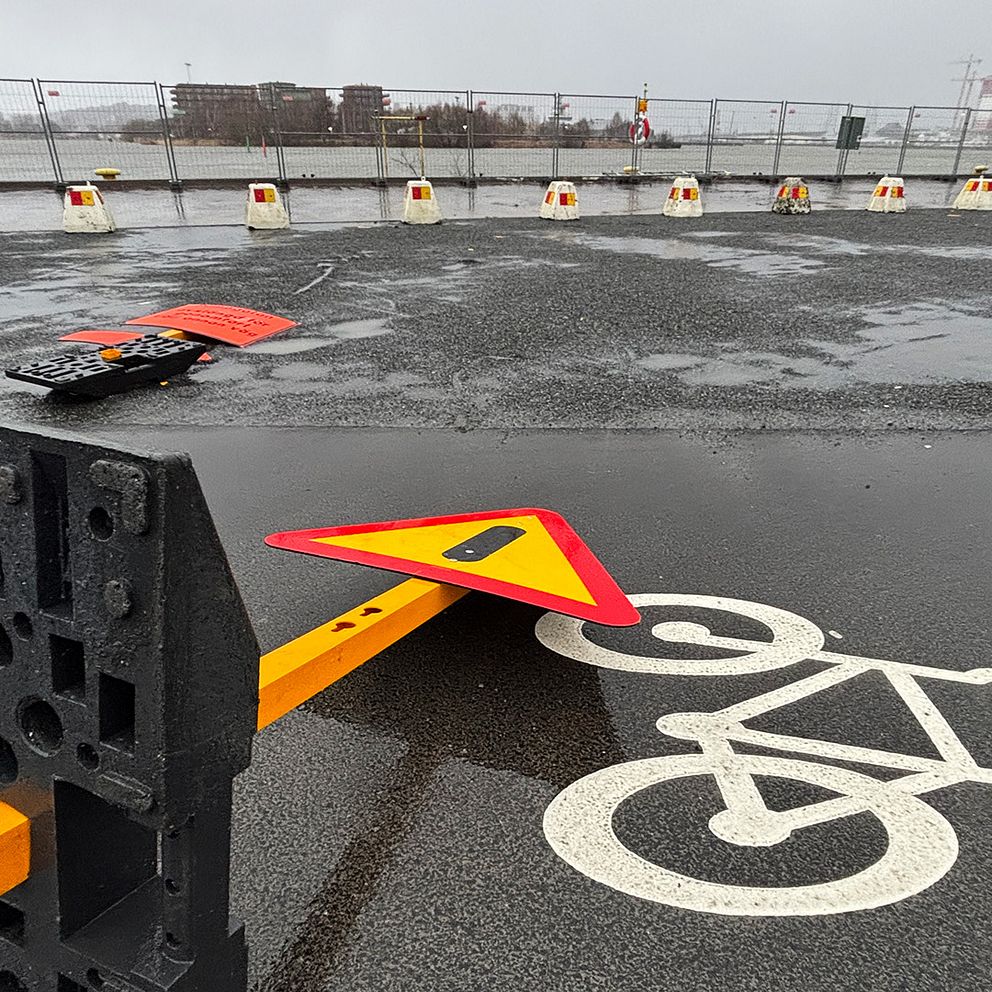 En vägskylt som har vält på en cykelbana i Göteborg, med regnvattensamling på asfalt. I bakgrunden syns cykelbanemärke och avspärrningar.