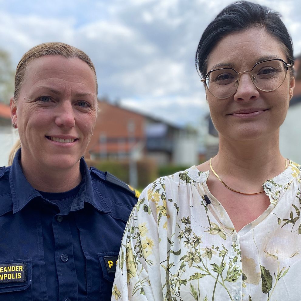 Två personer står utomhus, en i polisuniform och en i mönstrad blus. Hus syns i bakgrunden.