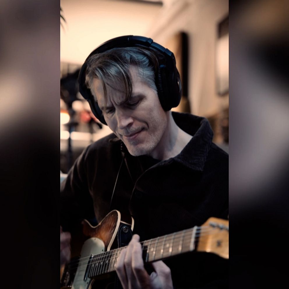 Person spelar elgitarr, klädd i mörka kläder, inomhusmiljö.