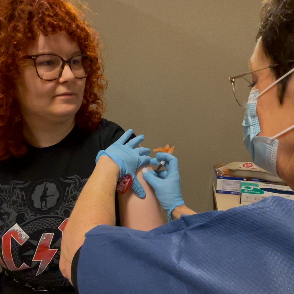 En ung kvinna får sin vaccinspruta av en sjuksköterska med munskydd