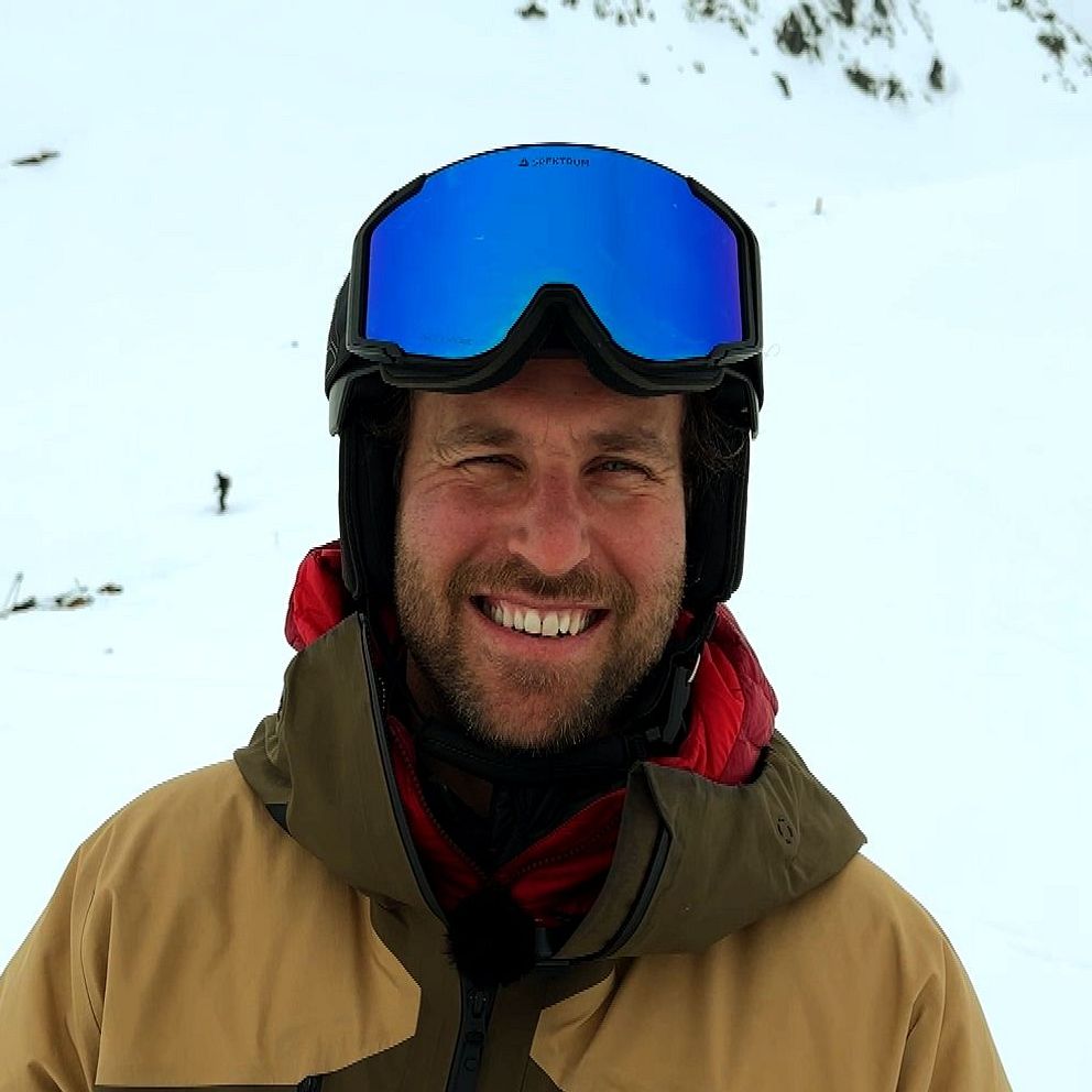 Person med skidkläder och hjälm på snötäckt fjäll.