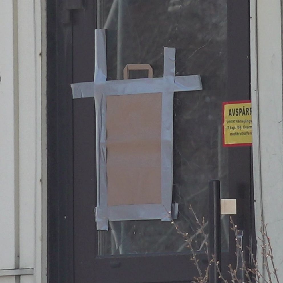 En entrédörr till ett bostadshus med krossad glasruta som har täckts över med kartong fasttejpad med silvertejp. Bredvid dörren sitter ett kodlås.