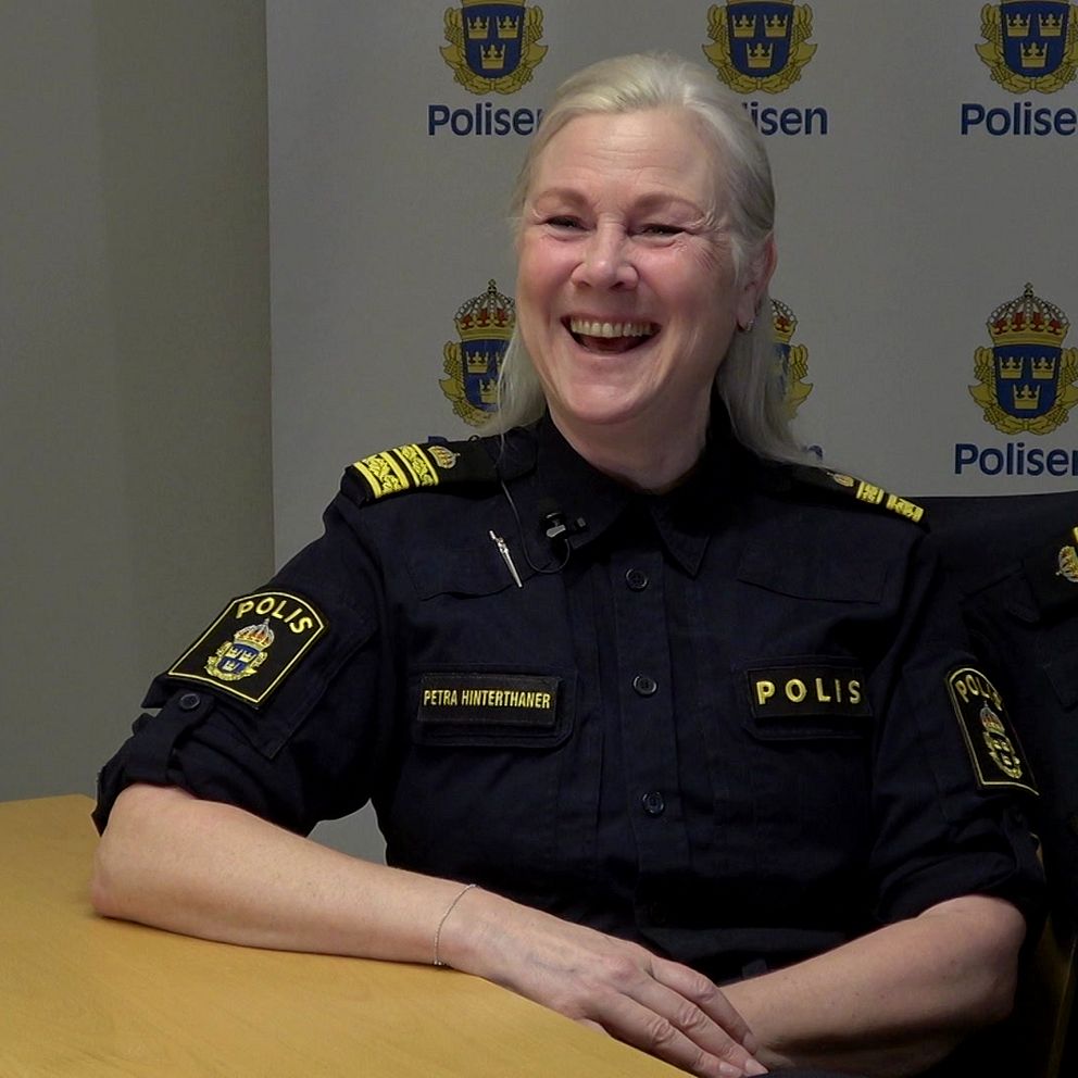 Polis i uniform sitter vid ett bord med polisens bakgrund.
