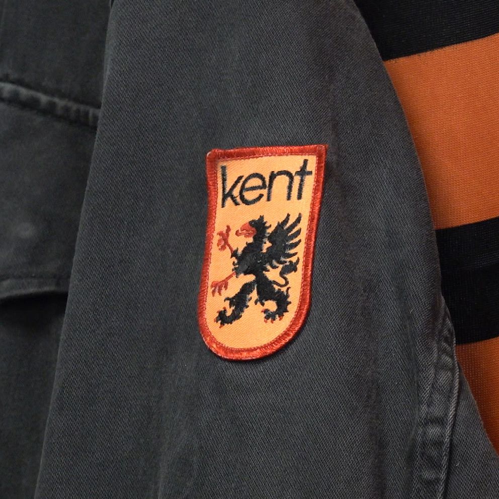 Svart jacka med Kent-tygmärke bredvid orange tyg med svarta ränder.
