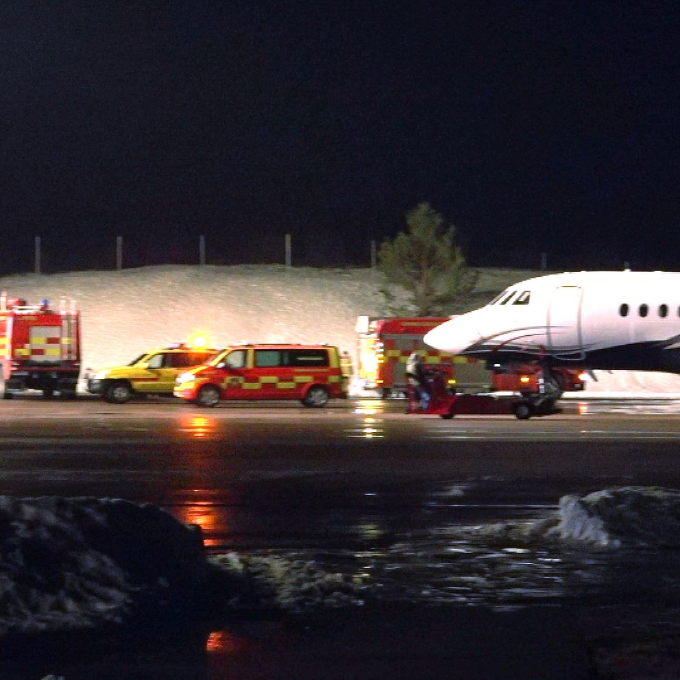 Räddningstjänst och ambulanser är närvarande vid en privatjet på en flygplats under natten, med snö på marken och tända ljus från nödbilarna.