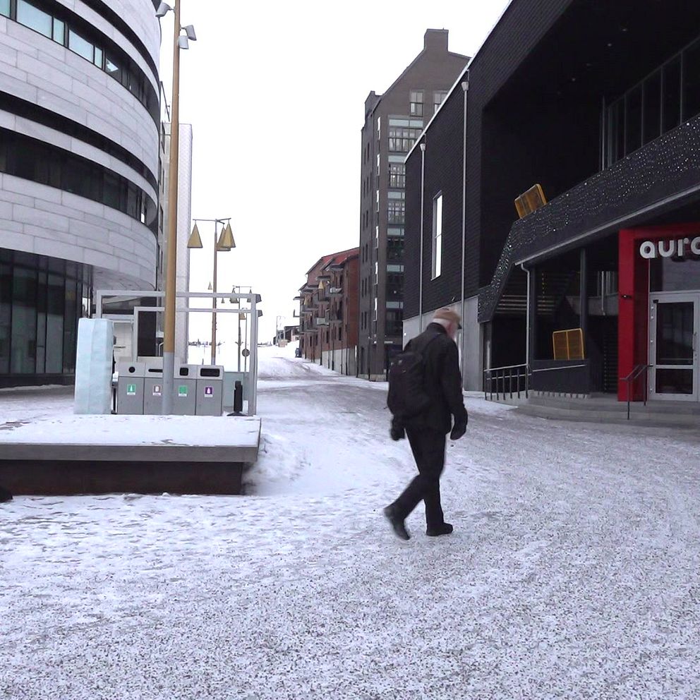 En man går genom en snötäckt gata mellan moderna byggnader.