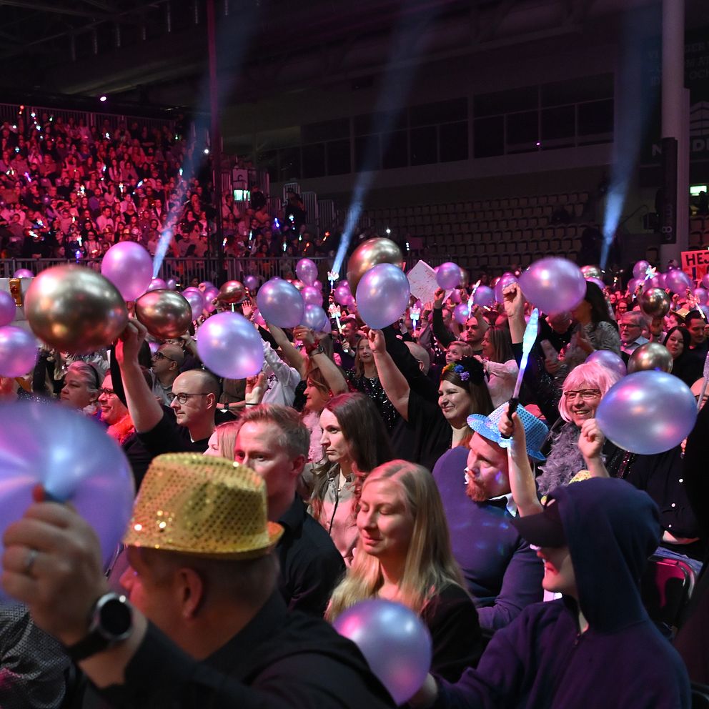 Publik på konsert, viftar med lysande ballonger i en fullsatt arena.