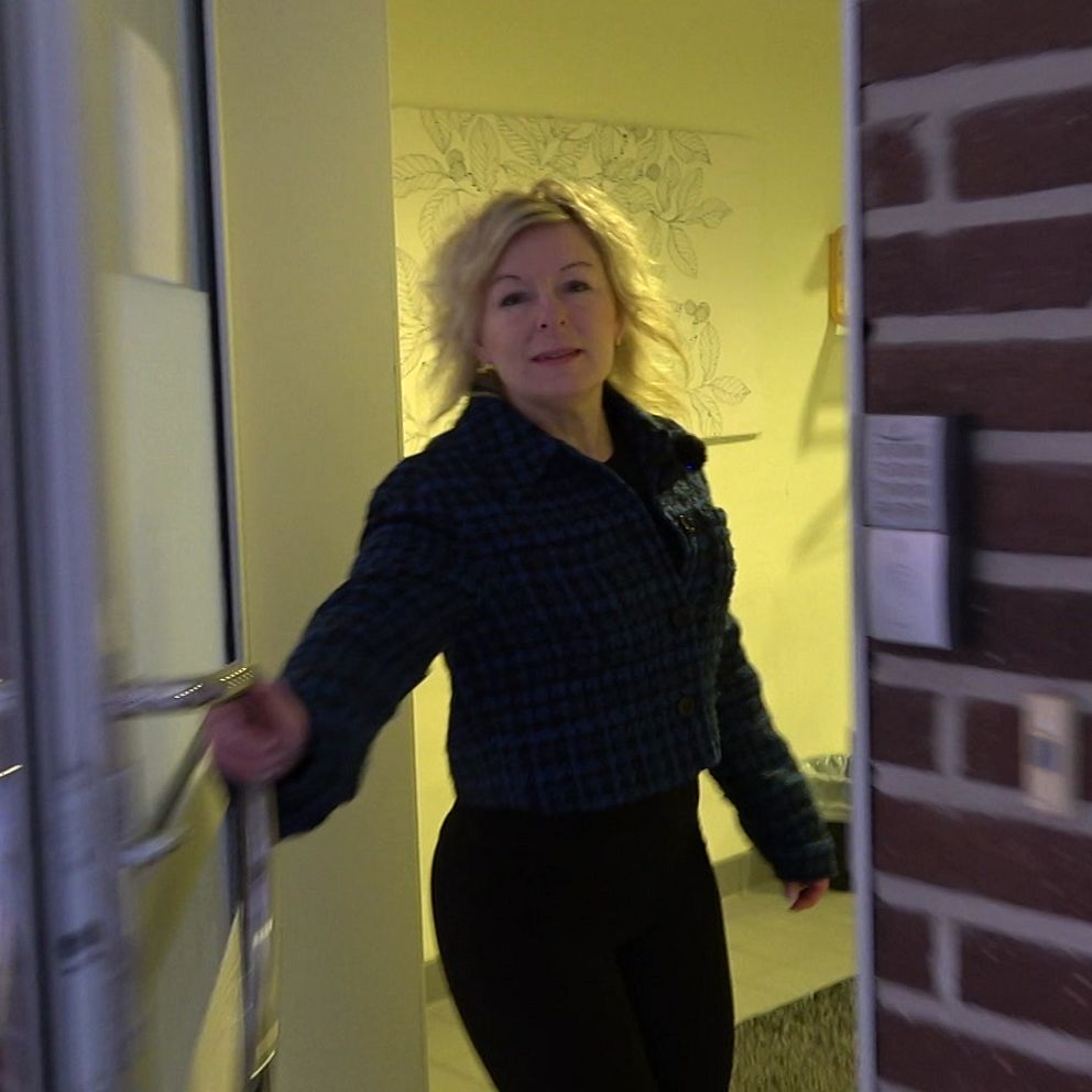 En person med ljus lockigt hår öppnar dörren till en byggnad med tegelväggar.
