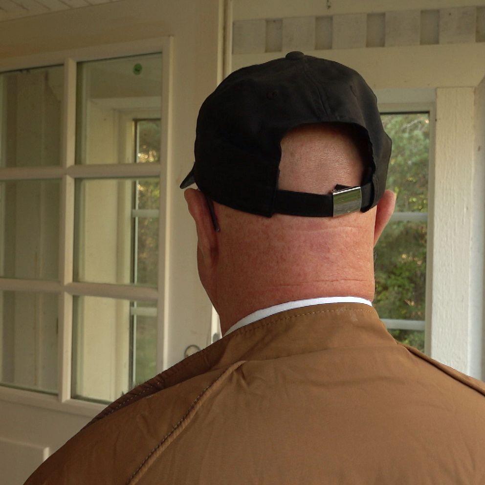 man bakifrån med svart keps och brun jacka vid en stugentré