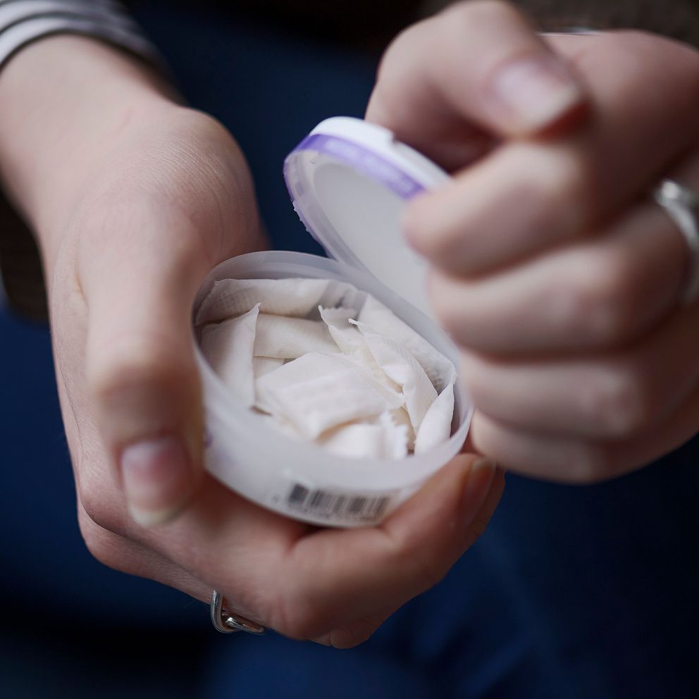 Hand håller en snusdosa fylld med vitt snus.