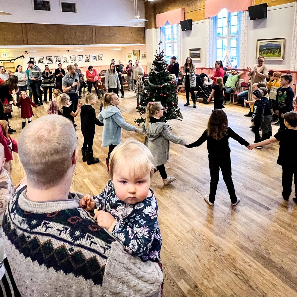En massa folk dansar runt en julgran i Tandsbyn