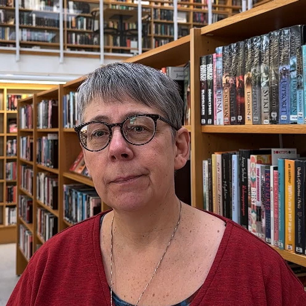 Person står i ett välfyllt bibliotek bland bokhyllor.