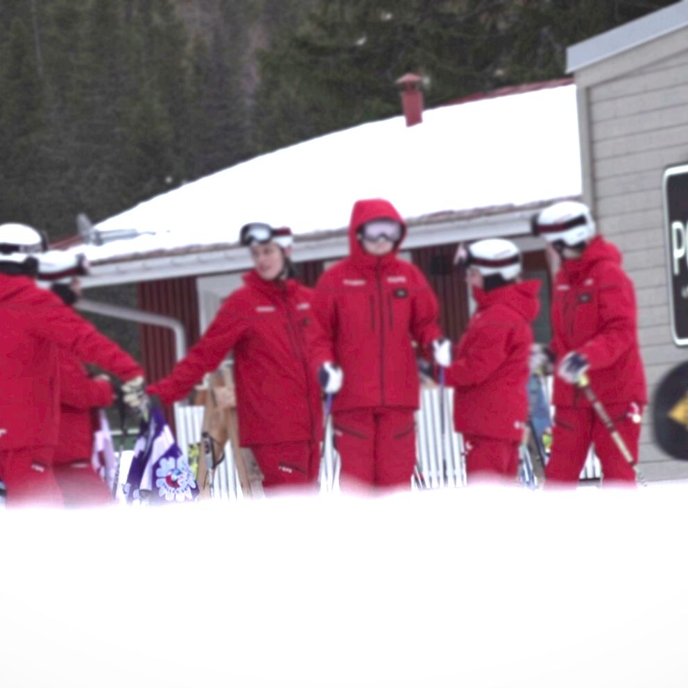En grupp skidlärare i röda jackor från Skistar står i rad utanför ett hus i Åre. De förbereder sig för att sätta igång med dagen.