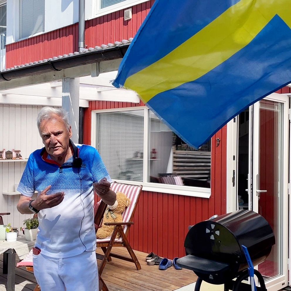 En man på en solig radhusaltan med en svensk flagga i förgrunden.