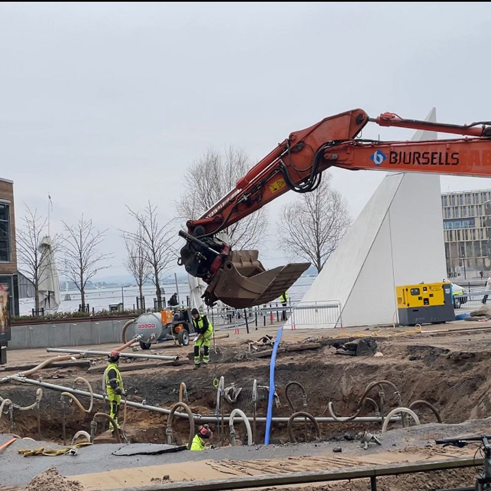 Grävmaskin arbetar på byggarbetsplats nära modern byggnad.