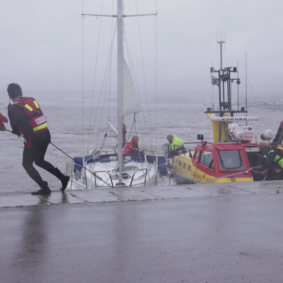Sjöräddningen står på kajen och drar i ett rep som är fastknutet i en segelbåt.