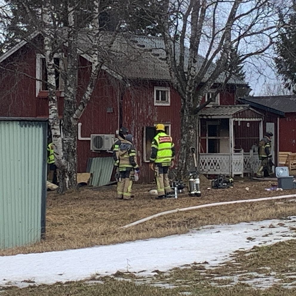 Brandmän undersöker rött hus med utrustning. Spår av snö på marken.