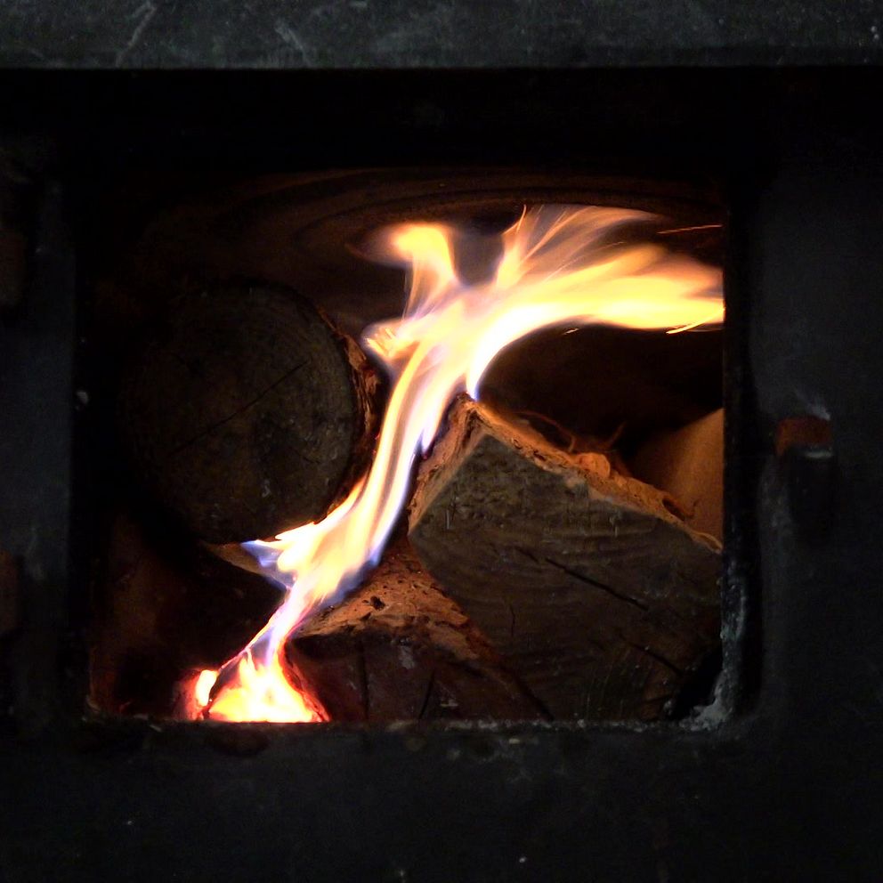 Brinnande ved inuti en vedspis, med synliga lågor som slår upp från stockarna.