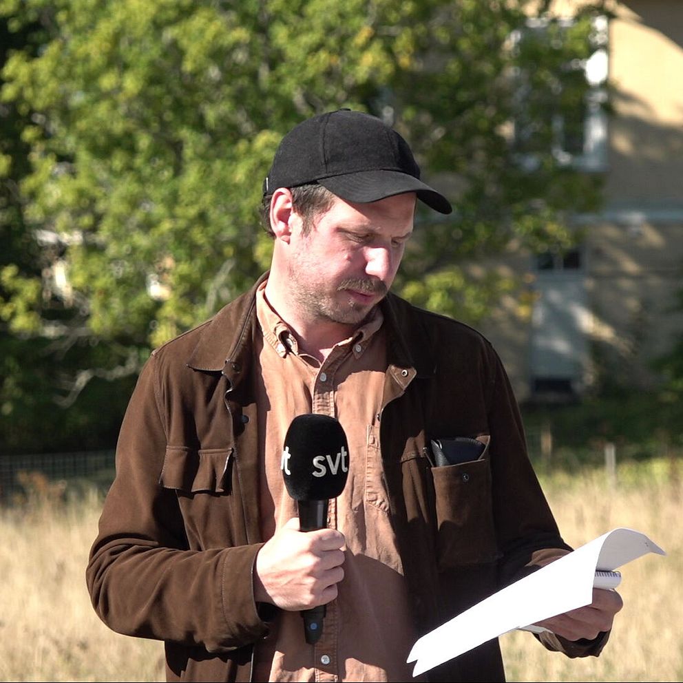 SVT:s reporter Albin Aghamn läser ett dokument utomhus i solen