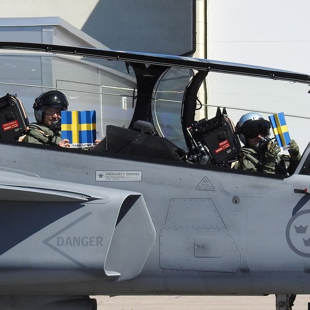 Ett Jas-plan med två piloter som viftar med svenska flaggor