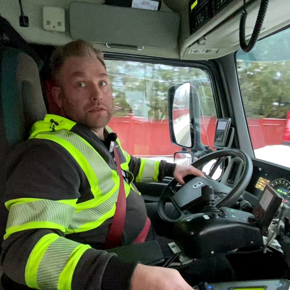 Henrik Danielsson iklädda reflexgula kläder, sitter i förarhytten på en lastbil i Luleå.