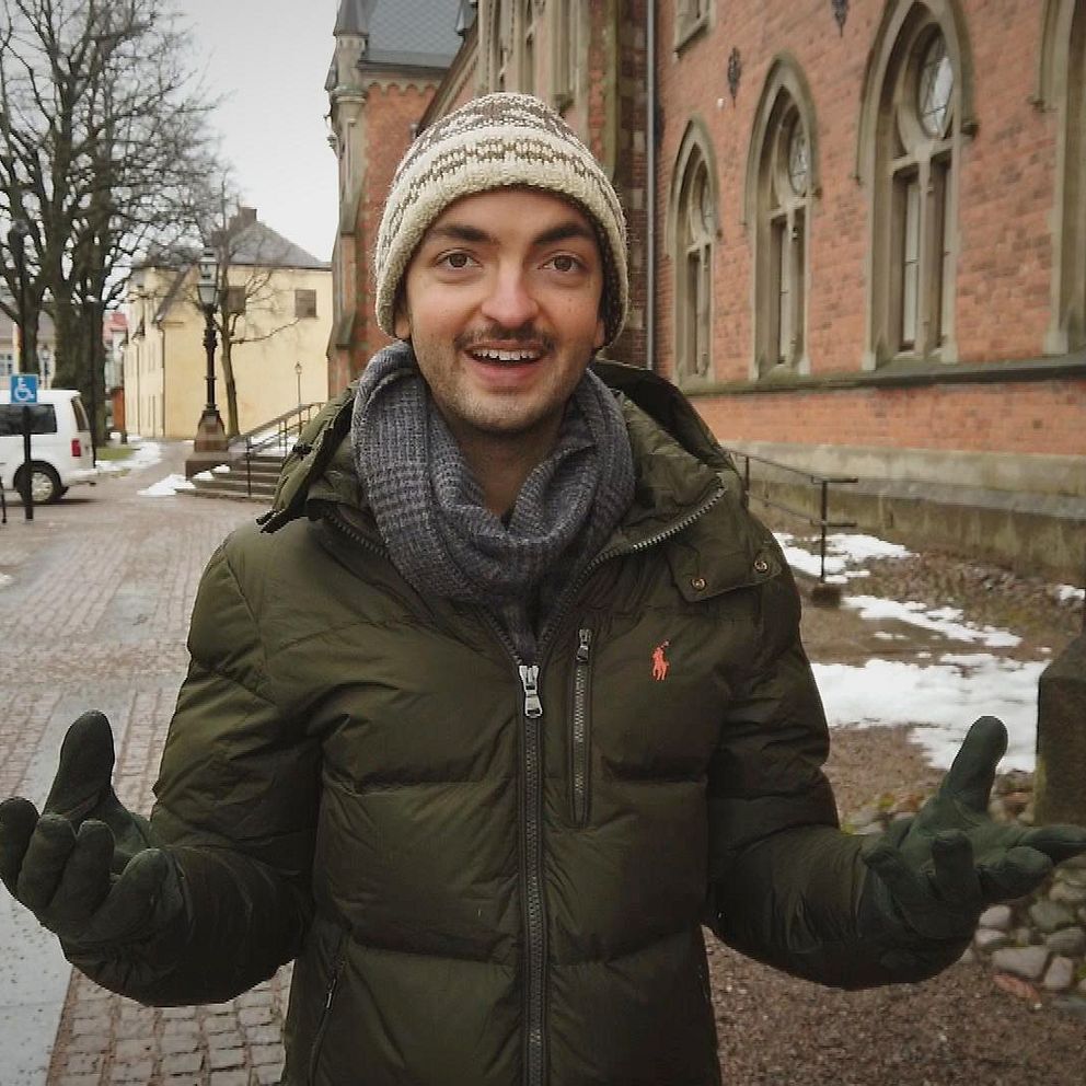 Jonathan Naraine i grän jacka och vitbrun mössa utanför röd gammal tegelbyggad (stadshuset i Skara)