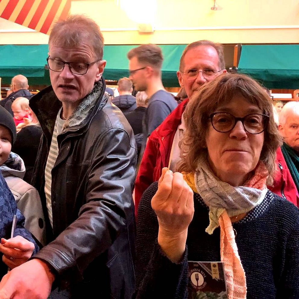 Människor står på en matfestival inomhus i Halmstad, pekar, provsmakar och tittar runt.