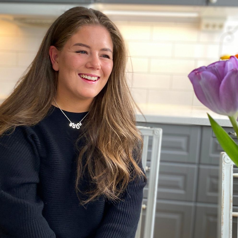 Nike leende vid köksbordet bredvid en vas lila tulpaner.