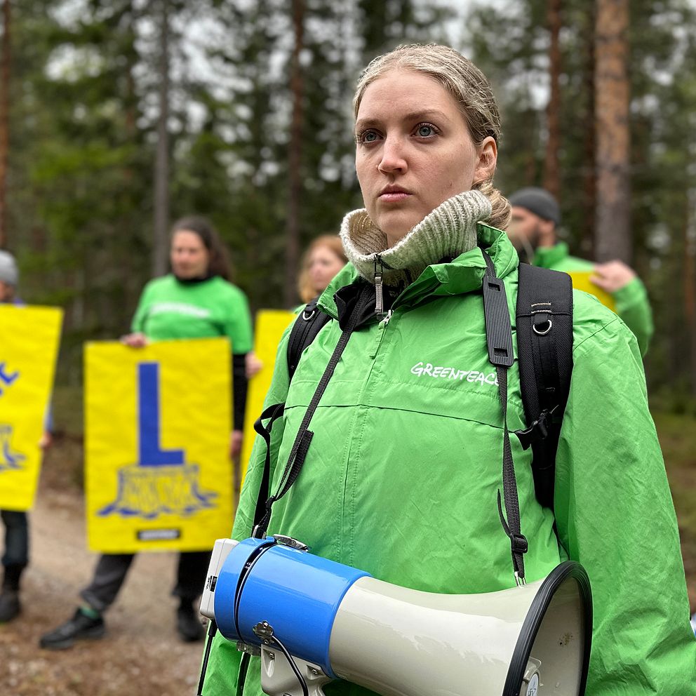 Kvinna med grön jacka står i skogen