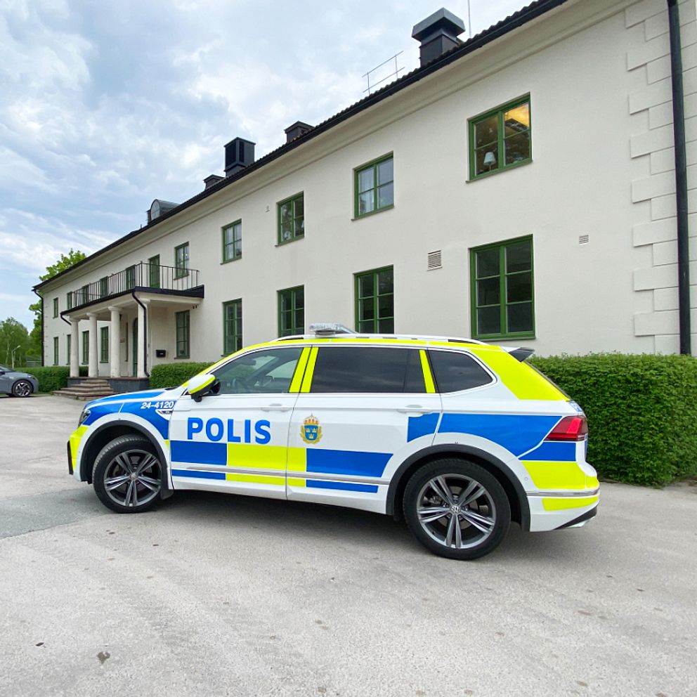 Polisbil står parkerad utanför en vit, äldre byggnad, där det drivs ett sis-hem.