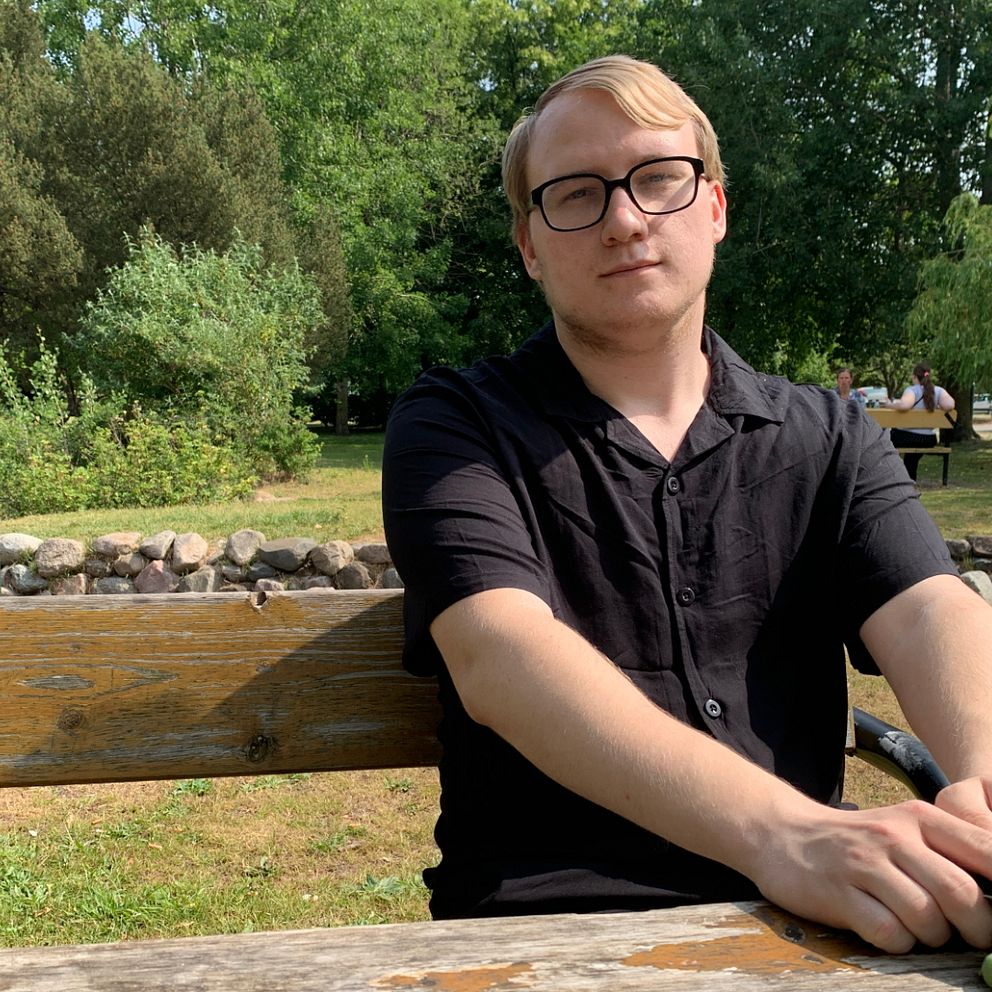 Marcus som sitter på en bänk med en park i bakgrunden.