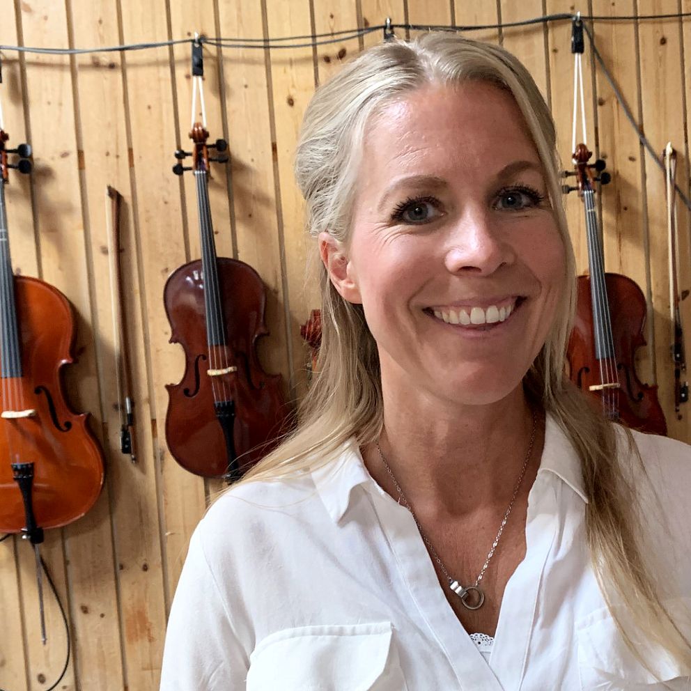 Kristin Kellander framför en massa fioler som hänger mot en vägg.