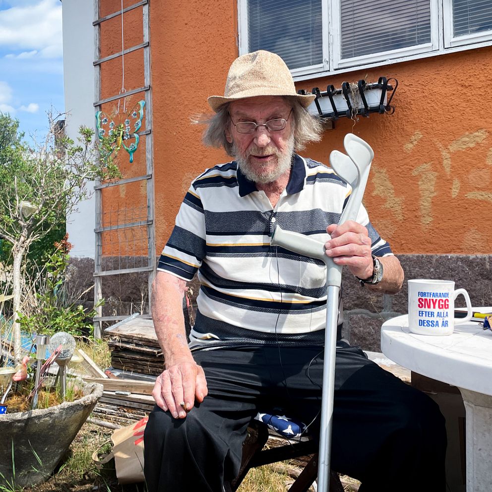Billy Tapper sitter utomhus vid ett plastbord. Han håller en krycka i handen.