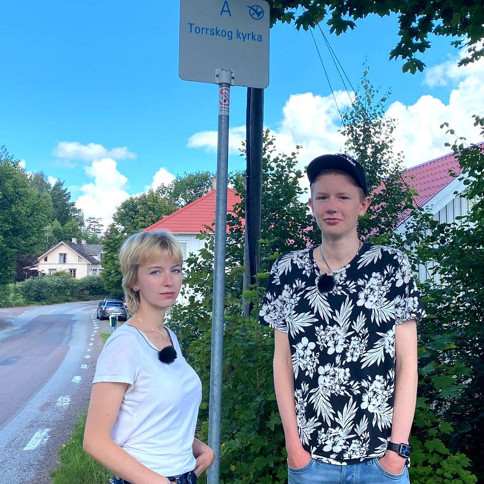 En tjej och en kille står vid en busshållsplats.