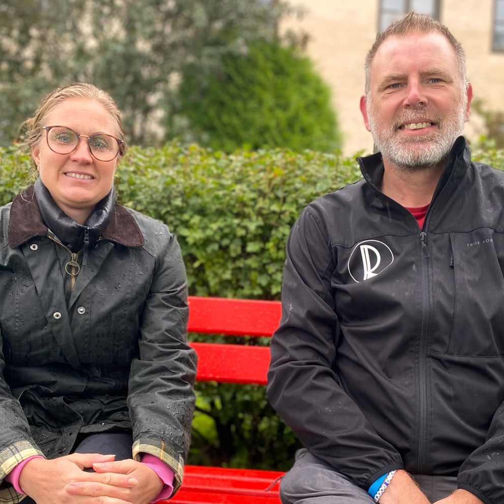 En kvinna, Frida Edholm (K) och en man, Richard Lindgren, sitter på en röd bänk på strandpromenaden i Vadstena.
