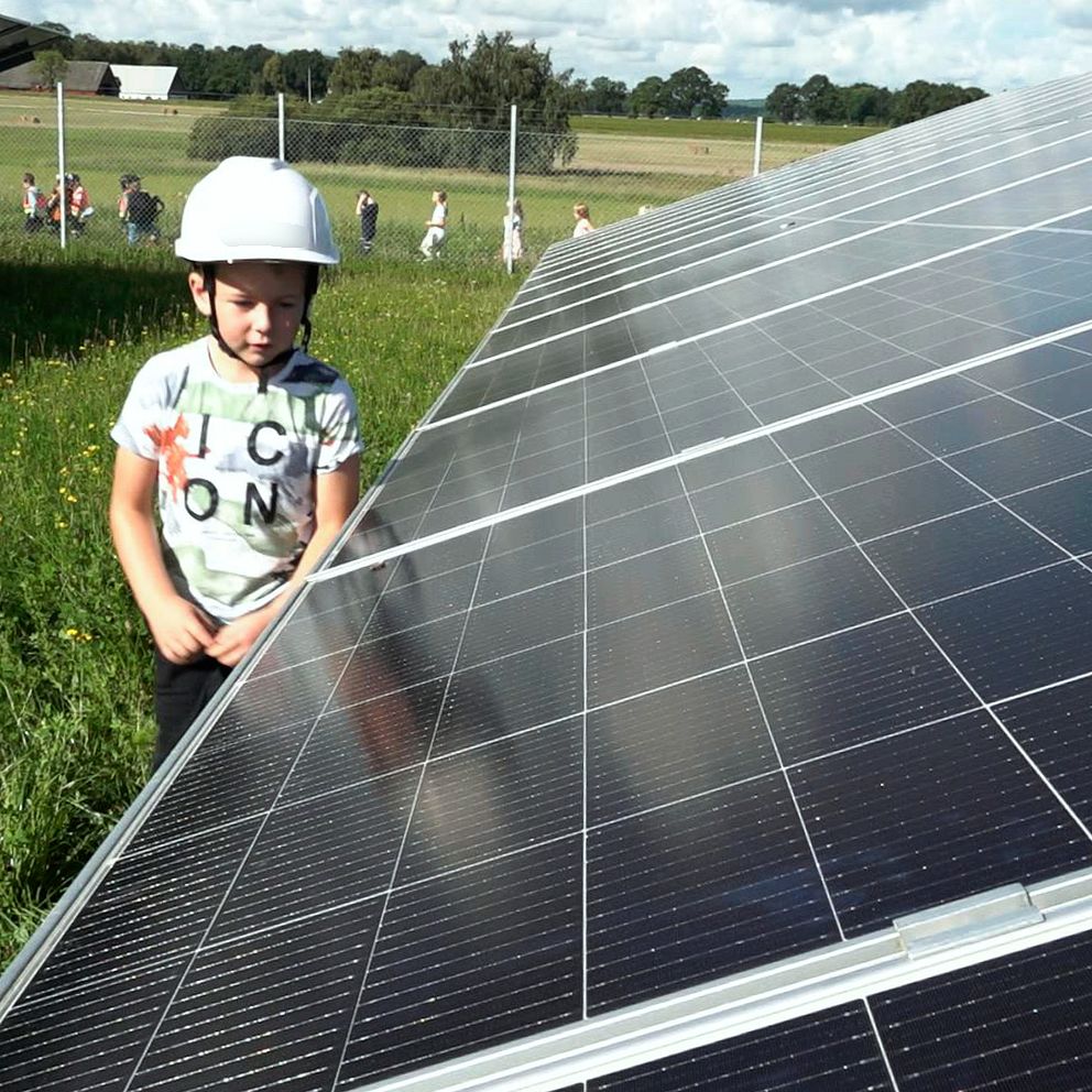 Första klass eleven Wegas Pegelow står bredvid flera solcellspaneler i Forsbys solcellspark.