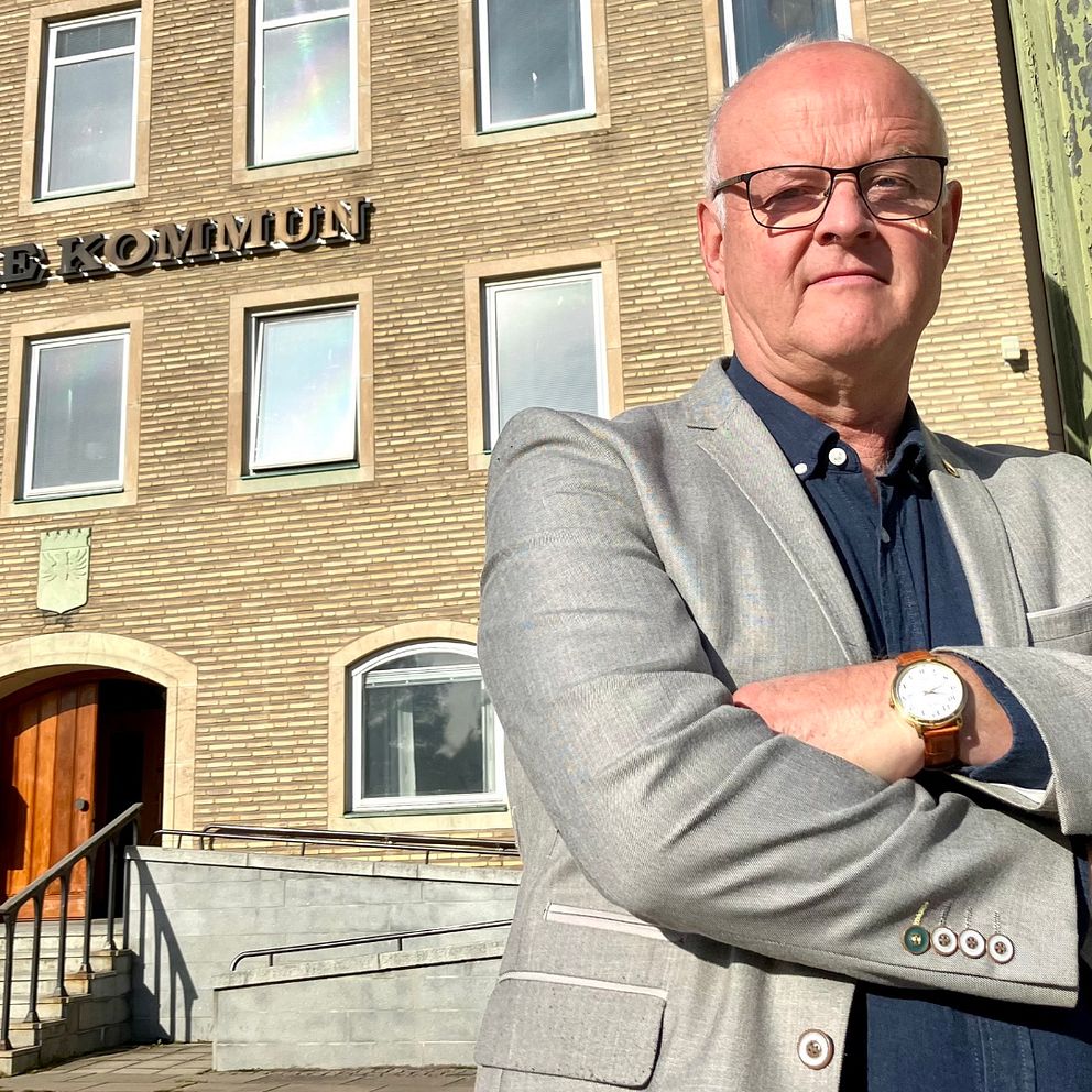 En man i ljusgrå kavaj och blå skjorta står med armarna i kors framför Säffles kommunhus.