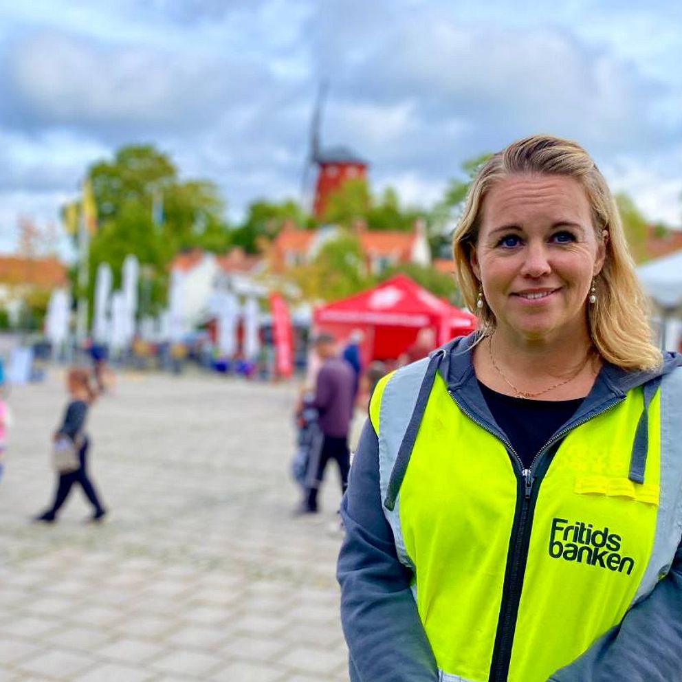 Kvinna i refelxväst på ett torg. människor i bakgrunden,