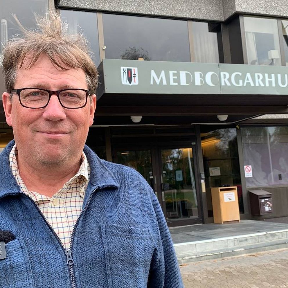 Man med brunt hår och glasögon står framför medborgarhuset i Sveg. Mannen har blå skjorta på sig.