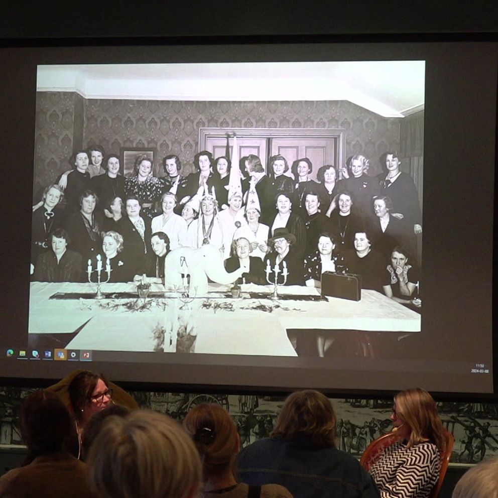 Bild på kvinnor i grupp på storskärm, inne på stadsmuseet