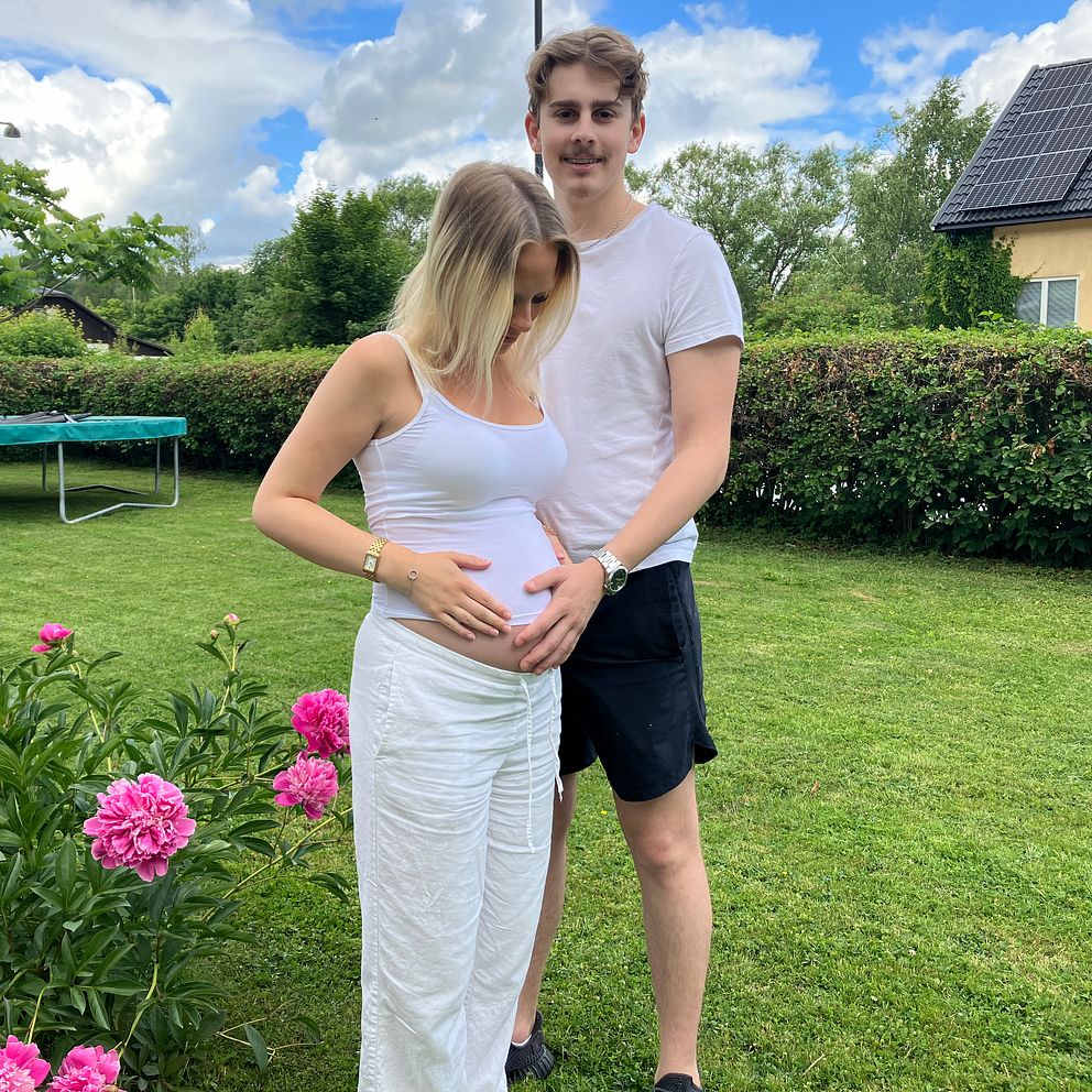 En man står bakom en gravid kvinna och håller sin hand på hennes mage