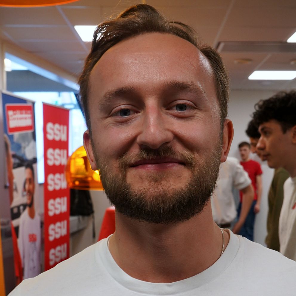 Ung man med kort skägg och kort hår tittar in i kameran.