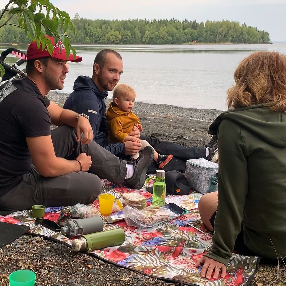 Familj sitter och fikar i skogen vid sjön
