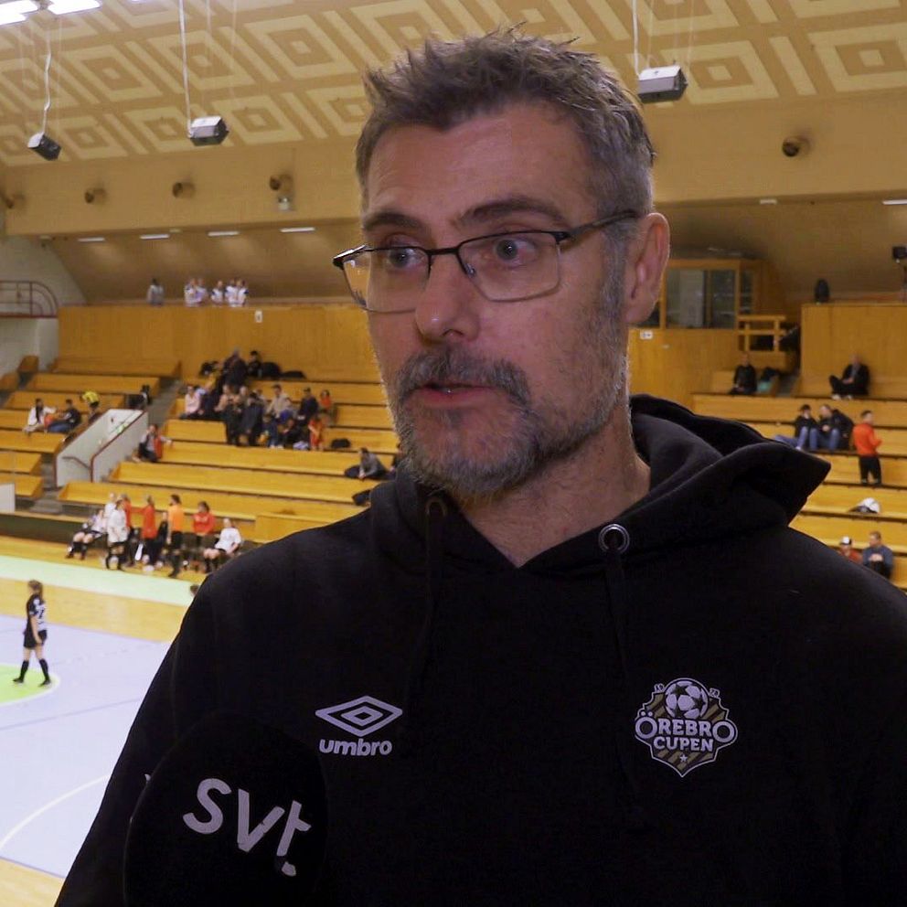En man syns i förgrunden och i bakgrunden spelar ungdomar fotboll i en inomhushall i Örebro.