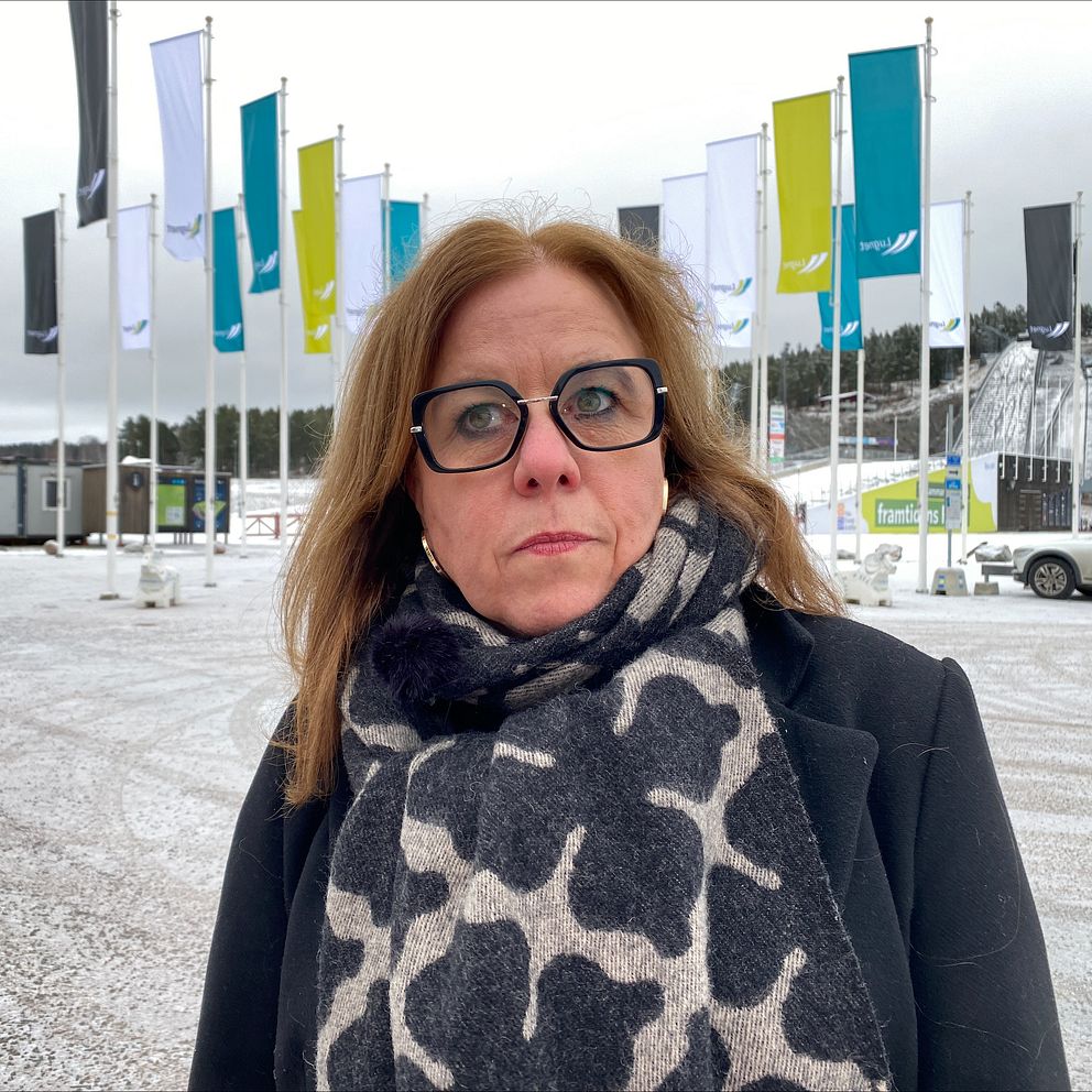 Ulrika Gustavsson, tf förvaltningschef kultur- och fritidsförvaltningen på Falu kommun, står framför en parkering som är täckt med ett tunt lager snö. En bil finns parkerad i bakgrunden och två hoppbackar syns på håll, och på parkeringen finns många flaggstolpar med flaggor som det står Lugnet på.